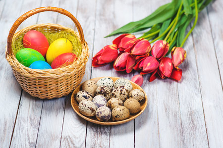 Easter background. Colored easter eggs and red tulips on the wooden background. Selective focus.