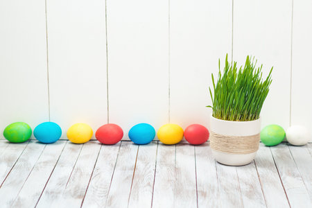 Colored easter eggs, flower pot with green grass on the wooden background. Space for text. Selective...