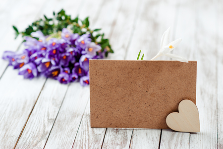 Beautiful crocus flowers in a basket near empty card for your text on the wooden background.の写真素材