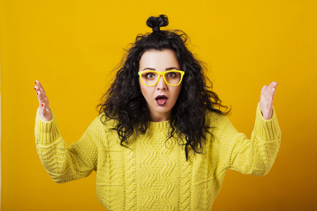Surprised young woman in glasses with modern hairstyle over the yellow background.の写真素材