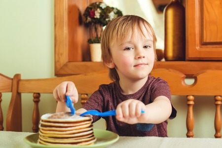 Cute little boy eating a stack of pancakes in kitchen.の写真素材