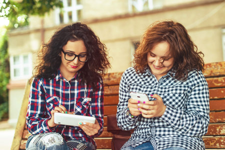 Two young women using tablet computer and a mobile phone outdoors.