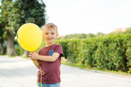 Little funny boy play with a yellow balloon outdoor.