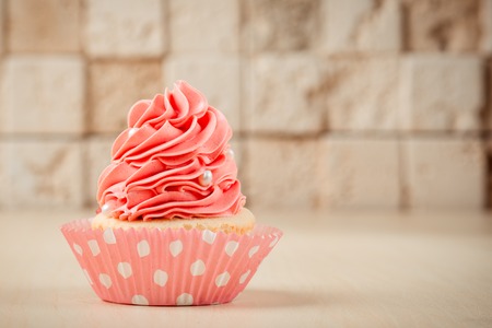 Pink tasty cupcake on table on the brick wall background.の写真素材