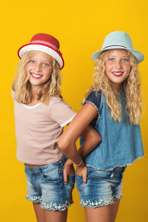Portrait of handsome young twins girls in summer hats, posing on the yellow background.の写真素材
