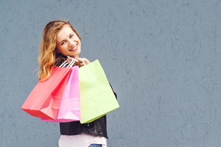 Joyfull casual woman holding shopping bags over grey background.の写真素材