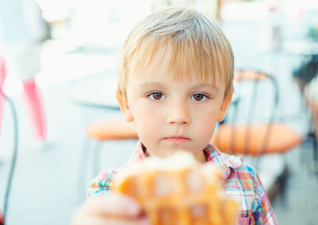 Cute little boy eats tasty belgian waffle on the summer terrace.の写真素材