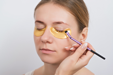 Beautiful young woman with gold hydrogel patches under eyes, isolated on the white. Skin care concept.の写真素材