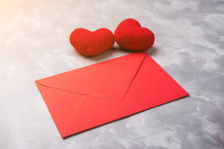 Red envelope and two knitted hearts on the grey textured background. Valentine day concept.