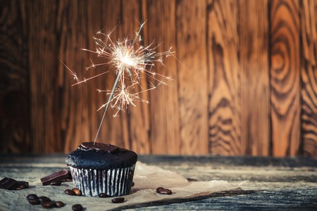 Chocolate cupcake with a sparkler on the wooden background.の写真素材