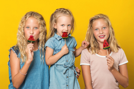 adorable funny little girls with lollipops, posing on yellow backgroundの写真素材