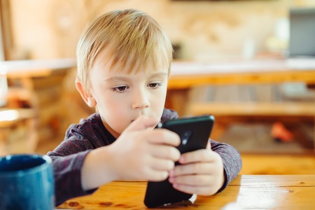Cute little boy playing games on the smartphone at home.の写真素材