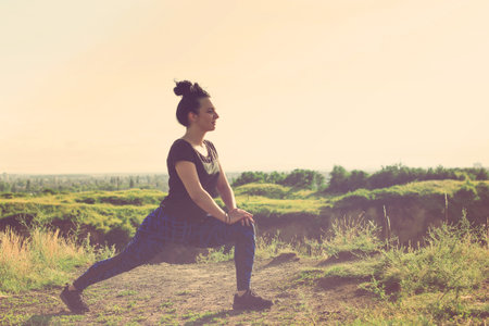 Beautiful young woman doing exercises on hill over city, outdoors sports