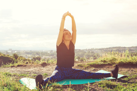 Attractive young-woman doing exercises on hill over city at sunset.