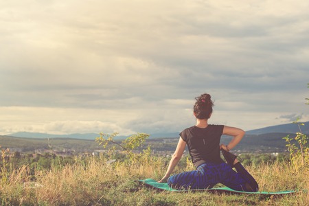 girl doing yoga exercise on top of the hill, back viewの写真素材
