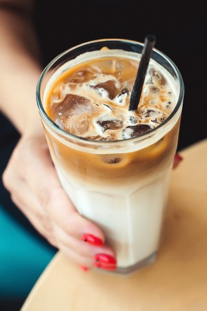 Iced coffee latte. Iced coffee with milk. Woman holding glass cup of iced coffee. Coffee time in summer day. Morning mood. Top view.の写真素材