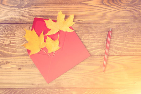 Red envelope with autumn leaves. Autumn letter. Maple leaves in red envelope, red pen on wooden...