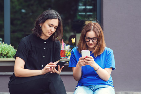 Pretty girls using smartphone .girls on their social network with mobile phone outdoors. Youth people addiction to new technology. People and technology conceptの写真素材