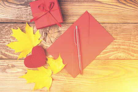 Colorful autumn background. Red envelope and maple leaves. Autumn mood. Small gift box, knitted...