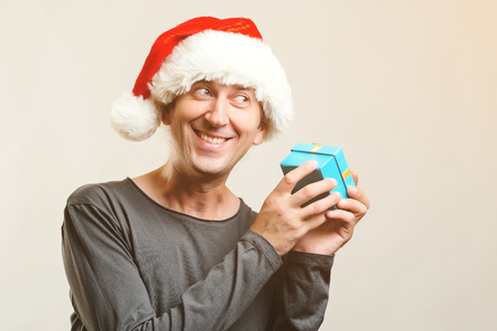 Funny guy with christmas hat holds small present. New Year Holiday. Christmas, x-mas, winter gifts concept. Man wearing Santa Claus hat, isolated on white. Copy space. Winter sales.の写真素材