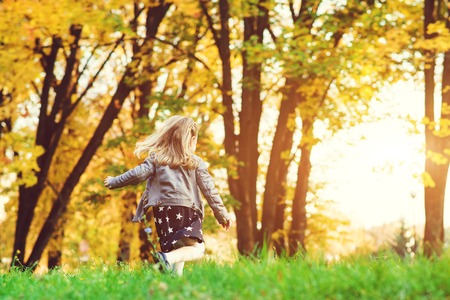 Happy child girl running in autumn park. Little girl having fun in autumn. Happy childhood. Stylish girl playing in the city park. Autumn kids fashion. Seasonal salesの写真素材