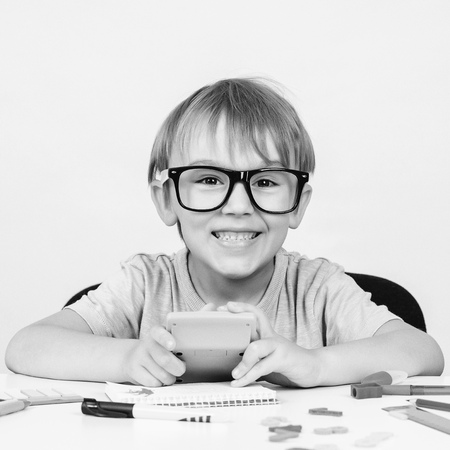 Happy smart boy in big glasses, sits at desk, looking to camera. Education. Kids idea. Genius. Back to school. Funny child in glasses doing his homework. Little boy has idea. Black and white imageの写真素材