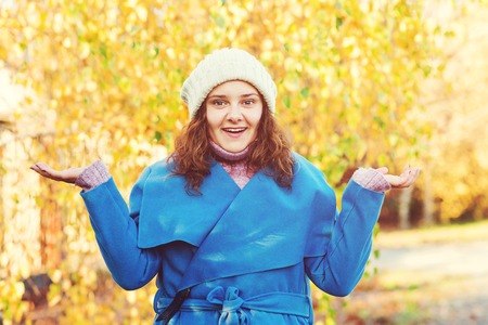 Surprised woman at autumn park, presenting something on empty palms. Autumn season. Woman in blue coat and knitted hat enjoying autumn. Woman autumn fashion. Expressive facial emotions. Copy spaceの写真素材