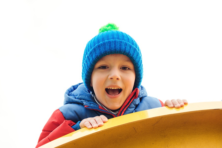 Adorable cute boy playing on playground on a cold day. Child wearing funny hat and red jacket. Funny little boy outdoors. Kids outdoors activities and leisure. Happy and healthy childhood. Happy babyの写真素材