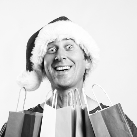 Christmas man. Man holding shopping bags. Christmas sales. Man wearing Santa claus hat in shopping time. New year holidays. Christmas gifts. Excited man in claus hat at christmas shopの写真素材