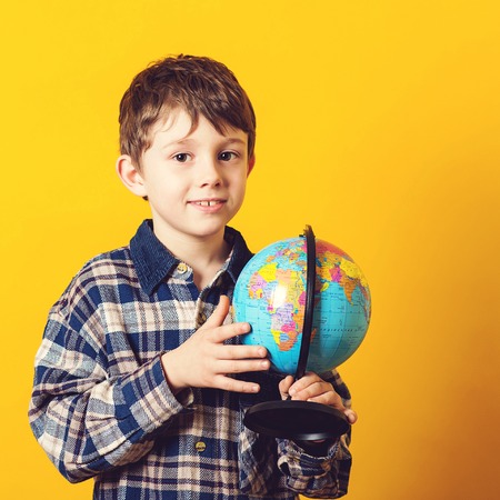 Curious boy holding earth globe map. Little traveler, isolated on yellow. Kid exploring the new horizons at globe. Funny kid with globe. Back to school concept. Educational globeの写真素材
