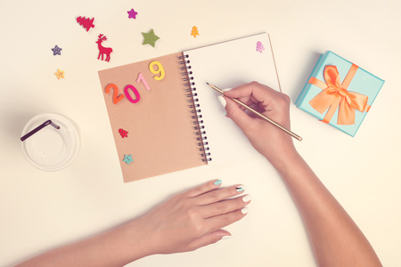 2019 goals list with notebook on white desk. Female hands are writing on notebook. Christmas planning concept . To do list. Mockup, copy spaceの写真素材