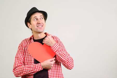 Funny man hugs a paper heart. Man in love. Handsome guy with red heart for his girl. Copy space....