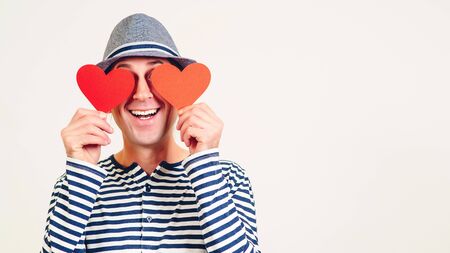 Happy Valentines Day. Funny man covers eyes with red hearts. Happy man in love. Romantic guy holds valentine cards. Be my valentine. Boyfriend showing love fun affection. Copy space.の写真素材
