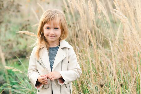 Adorable little girl smiling at walk. Fashionable child at nature at sunset. Happy child. Dream and freedom concept. Kids fashion. Little girl playing and enjoing warm summer eveningの写真素材