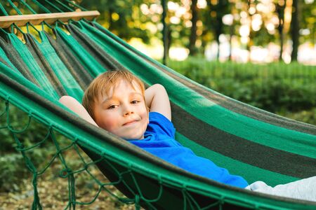 Happy child boy lying in a hammock in garden. Summer holidays concept. The child is resting in nature. Cute kid enjoy summer vacation with family at nature. Travel, vacation and lifestyle conceptの写真素材