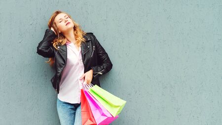 Stylish girl enjoying after great shopping. Shopper woman holding shopping bags. Girl posing against grey wall, copy space. Consumerism, shopping, sales and lifestyleの写真素材