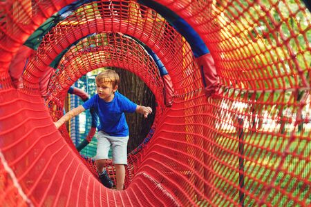 Happy kid overcomes obstacles in rope adventure park. Summer holidays concept. Little boy playing at rope adventure park. Modern amusement park for kids. Outdoors gamesの写真素材