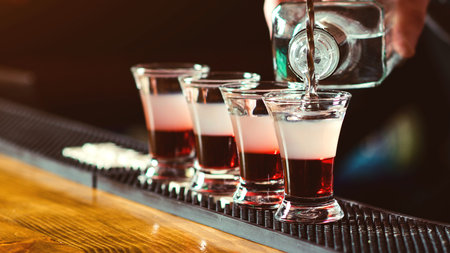 Bartender pouring strong alcoholic drink into small glasses on bar. Red shots at the nightclub....