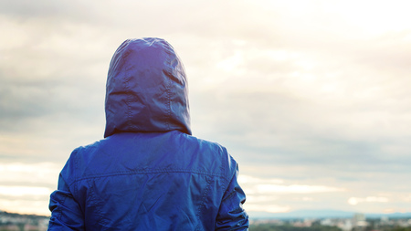 Back view of athlete woman looking sunset over city skyline after exercising. Motivation, sport and fitness lifestyle concept. Female tourist person in hooded jacket outdoors.の写真素材