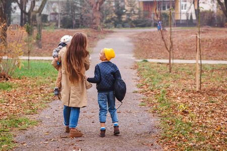 Happy mother and sons going to school and to kindergarten. Mother with two sons on walk in autumn. Back to school. Happy family in autumn parkの写真素材