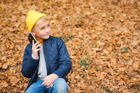 Stylish boy talking on cell phone outdoors. Kid on a walk in autumn park. People, technology and...