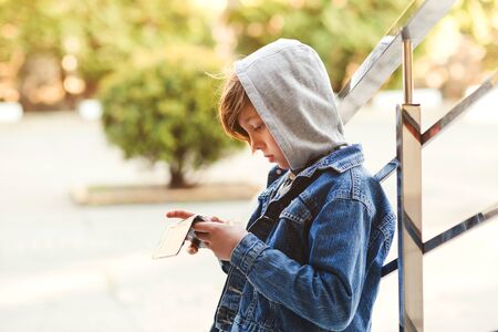 Preteen boy playing a game on the smartphone outdoors. Leisure, children, technology, internet communication and people concept. Kid boy with mobile phone outdoorsの写真素材