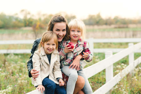Young mother and her little daughters on a walk at countryside. Happy family together on nature. Relationships, good mood and fashion conceptの写真素材