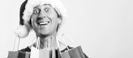 Excited young man in santa hat holding shopping bags. Christmas, sale, discount and holidays concept. Christmas crazy shopper with presents, on white background, copy spaceの写真素材