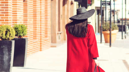 Autumn fashion. Elegant woman in red coat and stylish black hat, with trendy bag walking in city. Shopping day, great sales. People, shopping, travel and lifestyle.の写真素材