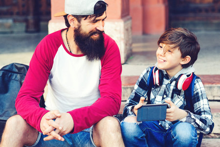 Happy young father with son sitting on stairs outside, having fun together. Schoolboy playing on...