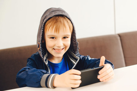 Happy boy playing games on mobile phone. Kid watching videos on smartphone at terrace outside....