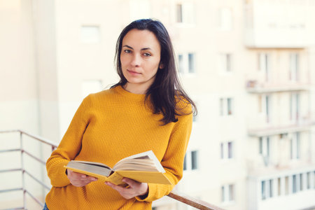 Pretty girl reading a book at balcony. Woman enjoys of rest. Home isolation. Coronavirus quaranrine. Time for reading. Lifestyle, people and leisure.の写真素材