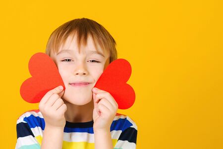 Cute child holding red hearts cards. Smiling boy with greetings card. Congratulations on Valentine's Day, Mother's Day, International Women's Day. Beautiful smile. Emotions. Love.の写真素材