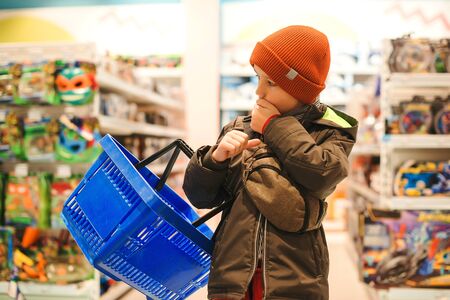 Little boy choosing toy in supermarket. Kid difficult to choose the best toy. Child with shopping basket at the toys shop. Christmas sales. Shopping and sales.の写真素材
